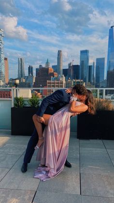 a man and woman kissing on top of a roof in front of the city skyline