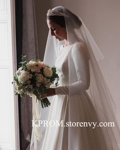 a woman in a wedding dress holding a bouquet and looking down at the floor with her veil over her head