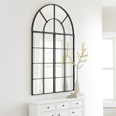 a white dresser sitting next to a window in a room with a mirror on the wall