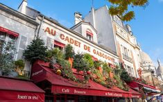 an outdoor cafe with red awnings and plants on the roof