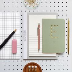 a desk with notebooks, pens and pencils on it next to a chair