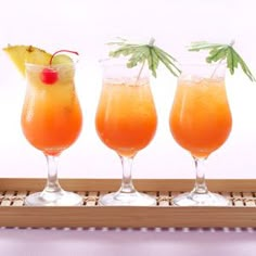 three glasses filled with orange juice and garnished with pineapple on a bamboo tray