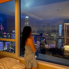 a woman standing in front of a window looking out at the city lights and skyscrapers