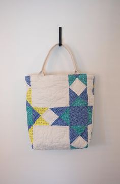 a blue and yellow quilted bag hanging from a hook on a wall with white walls