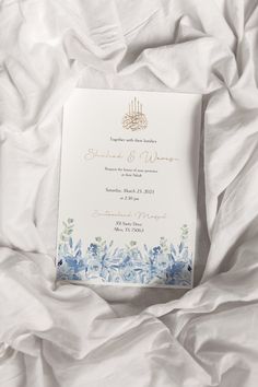 a white and blue wedding card laying on top of a bed