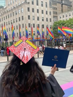 a person wearing a graduation cap and holding a book in front of them with flags behind her