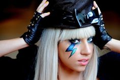 a woman with white hair and blue eyes is wearing black leather gloves and a hat that has lightning painted on it