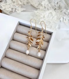 two pairs of gold leaf and pearl drop earrings in a gift box on a table