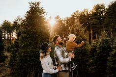 a man, woman and child standing in front of some trees with the sun behind them