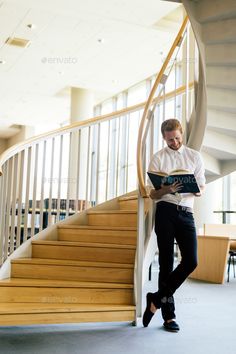 a man standing in front of a spiral staircase reading a book - stock photo - images