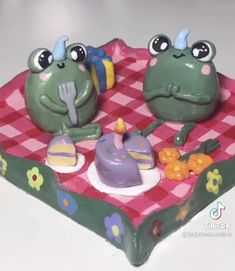 two frog figurines sitting on top of a pink and green checkered tray