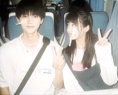 two people sitting on a bus holding up peace signs