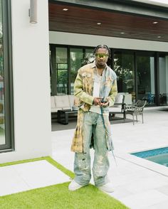 a man standing in front of a swimming pool wearing ripped jeans and a long coat