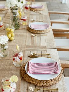 a long table with plates and glasses filled with watermelon slices, lemons, and strawberries