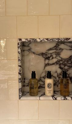 three bottles of hand soap and lotion sitting on a shelf in a tiled bathroom