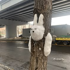 a white stuffed animal hanging from the side of a tree in front of an overpass