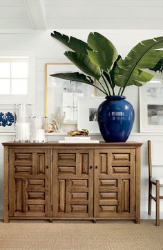 a blue vase sitting on top of a wooden table next to a wall with pictures