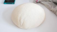 a ball of dough sitting on top of a white table next to a cell phone