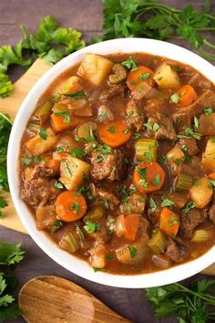 a white bowl filled with stew and carrots on top of a wooden cutting board