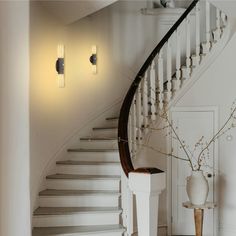 a white staircase with two lights and a vase on the floor in front of it