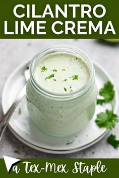 a close up of a jar of cream on a plate with cilantro and lime