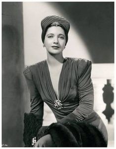 an old black and white photo of a woman sitting on a chair wearing a head scarf