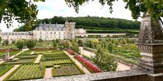 a large garden with lots of trees and flowers in front of a castle like building