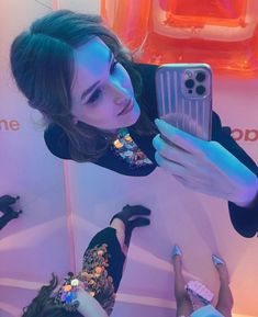 a woman taking a selfie with her cell phone in front of an orange wall