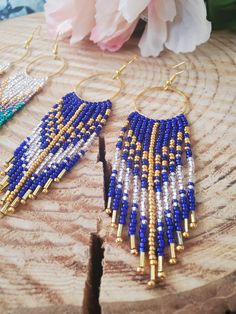 two pairs of beaded earrings on top of a piece of wood with flowers in the background