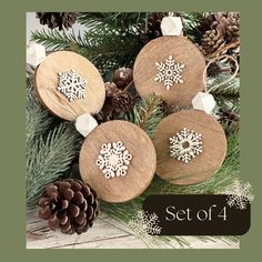 three wooden ornaments with snowflakes on them next to pine cones and evergreen branches