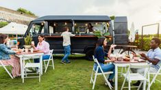 people are sitting at tables in front of a food truck that is parked on the grass