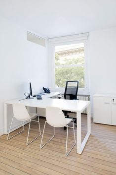 a white desk with two chairs and a laptop on it in an empty room next to a window