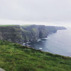 two people standing on the edge of a cliff overlooking the ocean with cliffs in the background