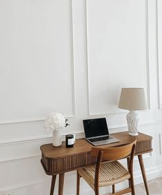 a laptop computer sitting on top of a wooden desk next to a vase with flowers