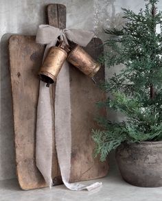 a wooden board with two bells attached to it next to a potted pine tree