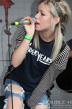 a woman singing into a microphone in front of a wall with an advertisement on it