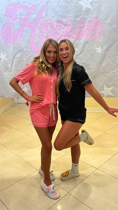 two young women posing for the camera in front of a pink and white sign with stars on it