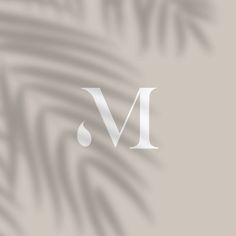 the letter m is shown in white on a beige background with palm leaves and shadows