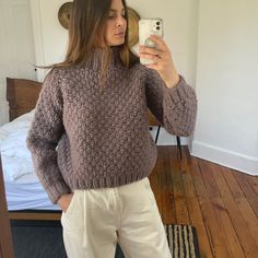 a woman taking a selfie with her cell phone while wearing a brown sweater and white pants