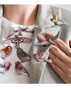 a woman holding several birds on her lapel and wearing a white shirt with silver buttons