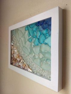 an art piece is hanging on the wall next to a white frame with sea glass in it