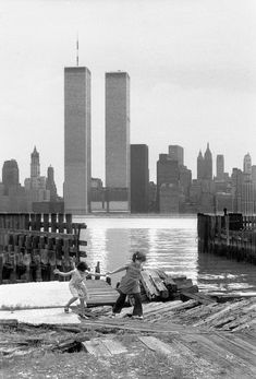 black and white photograph of children playing in the water near two tall buildings with skyscrapers in the background