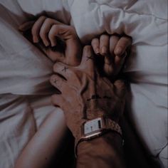 two hands holding each other while laying in bed