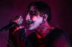 a man with tattoos and piercings on his face holding a microphone in front of him