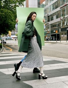 a woman is walking down the street with an umbrella over her head and holding up a green sign