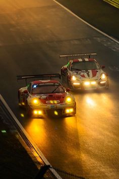 two race cars driving down the road in the rain at night with headlights shining on them