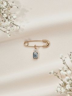 a gold pin with a blue stone on it next to some white flowers and branches