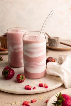 two strawberry milkshakes on a plate with strawberries and other food items in the background