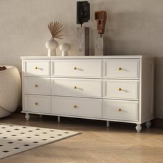 a white dresser sitting on top of a hard wood floor next to a rug and vases