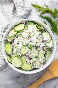 a white bowl filled with cucumbers and onions on top of a marble counter